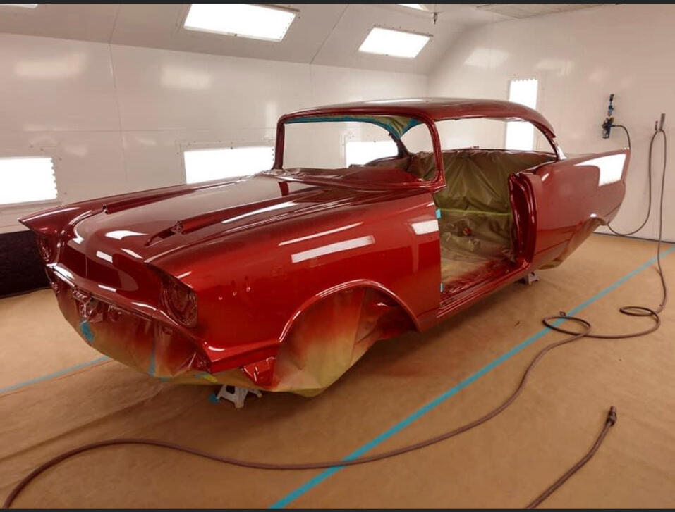 Vintage coupe resprayed in deep red inside a paint booth—fresh custom paint, masked and prepped for reassembly.