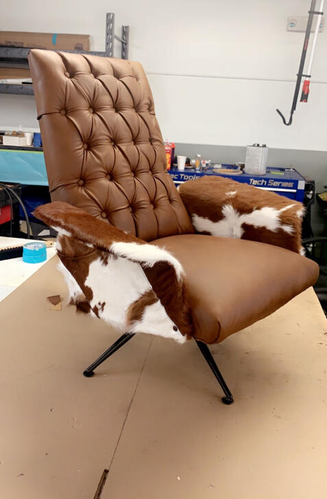 Custom lounge chair reupholstered in brown tufted leather with cowhide accents and black metal legs.